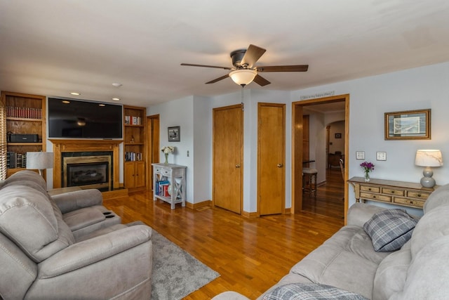 living room with a ceiling fan, a glass covered fireplace, baseboards, and wood finished floors