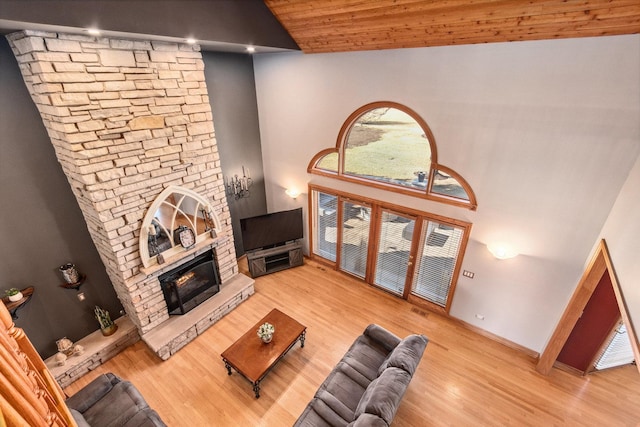 living room featuring wood ceiling, a stone fireplace, wood finished floors, high vaulted ceiling, and baseboards