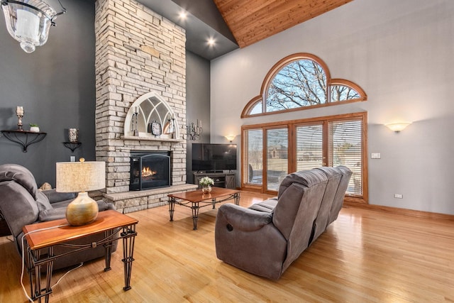 living area with light wood finished floors, high vaulted ceiling, and a stone fireplace