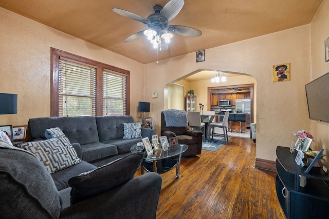 living room featuring arched walkways, a textured wall, dark wood-style flooring, and a ceiling fan