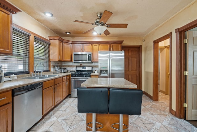 kitchen featuring brown cabinetry, a kitchen island, stainless steel appliances, a kitchen bar, and a sink