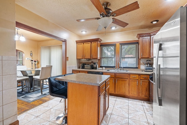 kitchen with brown cabinets, stainless steel refrigerator with ice dispenser, a kitchen island, a sink, and a kitchen bar