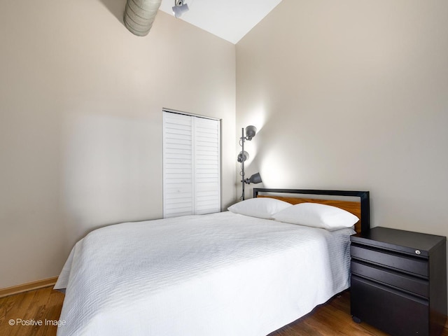 bedroom featuring a closet, high vaulted ceiling, baseboards, and wood finished floors