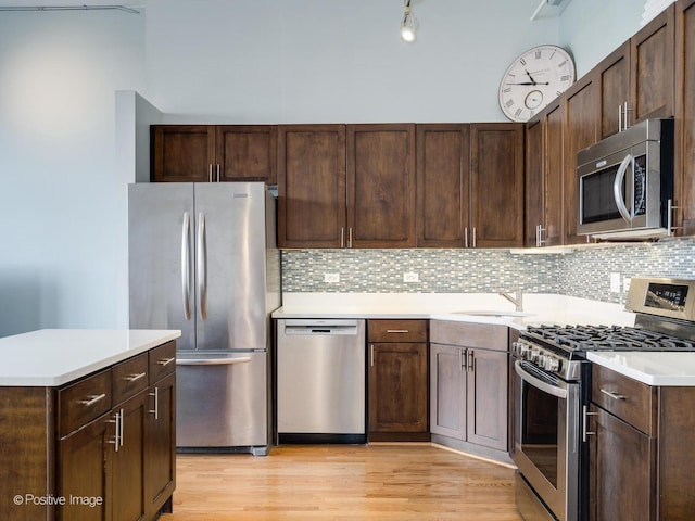 kitchen featuring dark brown cabinetry, light countertops, light wood-type flooring, decorative backsplash, and appliances with stainless steel finishes