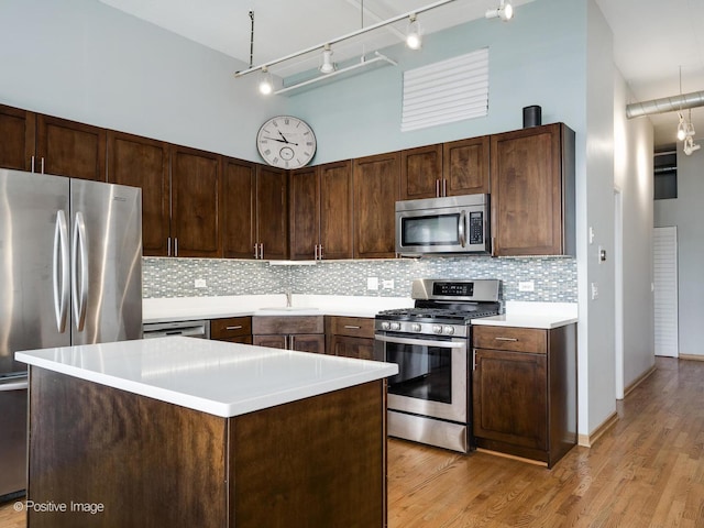 kitchen featuring backsplash, light wood-type flooring, appliances with stainless steel finishes, a towering ceiling, and a sink