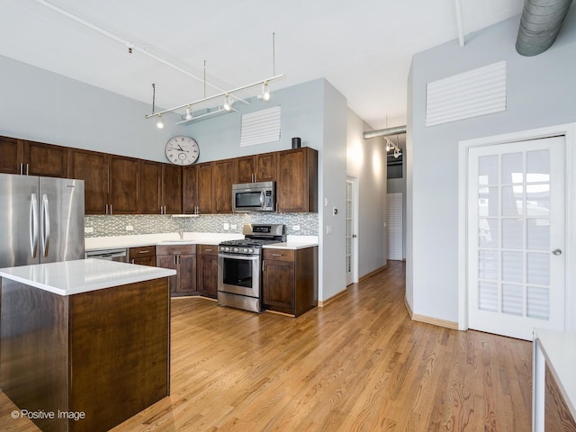 kitchen featuring light wood-style flooring, stainless steel appliances, dark brown cabinetry, light countertops, and tasteful backsplash