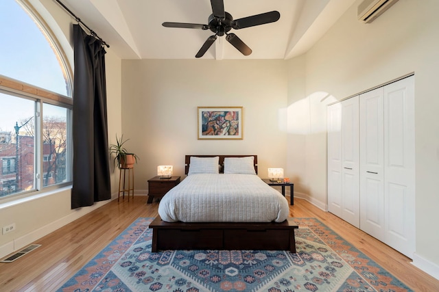 bedroom with light wood finished floors, a wall mounted air conditioner, visible vents, and baseboards