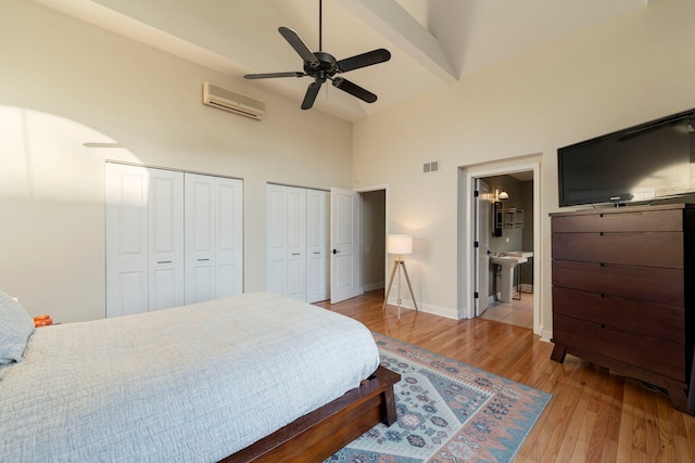 bedroom with baseboards, visible vents, wood finished floors, an AC wall unit, and multiple closets