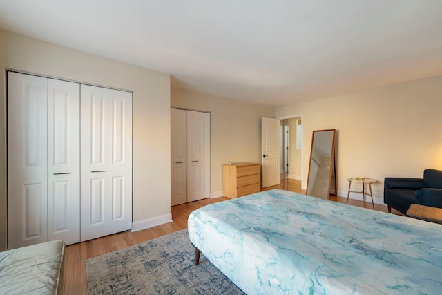 bedroom featuring baseboards, two closets, and light wood-style floors