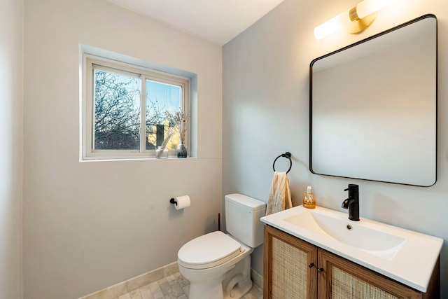 half bath with baseboards, vanity, and toilet