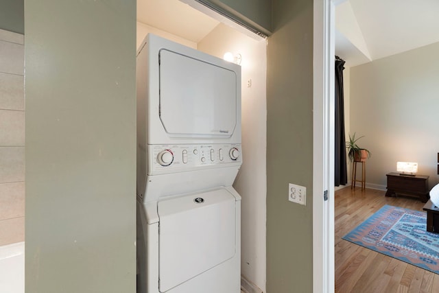 washroom with light wood-style floors, stacked washer / drying machine, laundry area, and baseboards