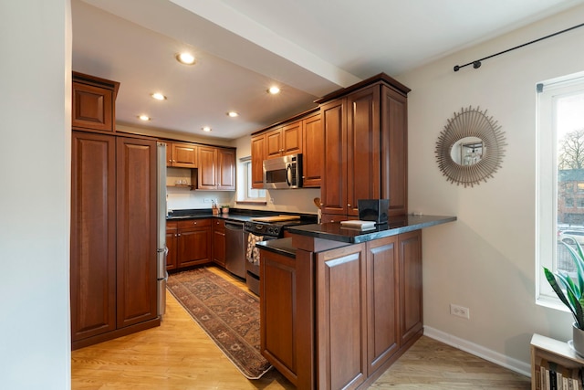 kitchen with stainless steel appliances, dark countertops, a peninsula, and light wood finished floors