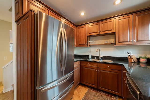 kitchen featuring appliances with stainless steel finishes, brown cabinetry, a sink, and light wood finished floors