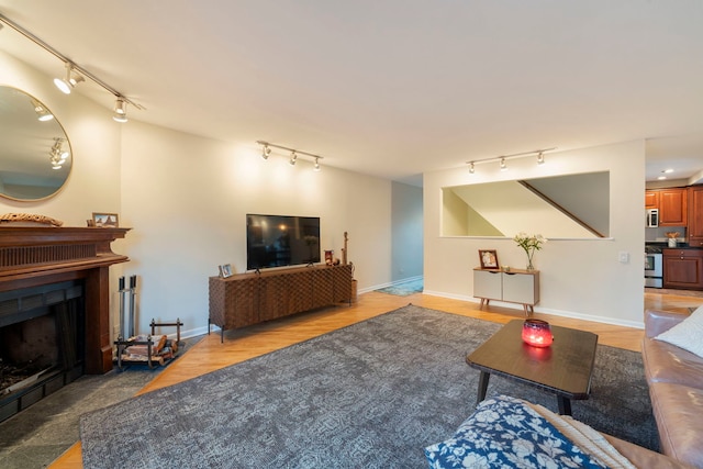 living area with a fireplace, rail lighting, light wood-style flooring, and baseboards