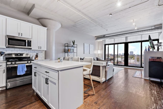 kitchen with dark wood-style floors, backsplash, appliances with stainless steel finishes, open floor plan, and a kitchen bar