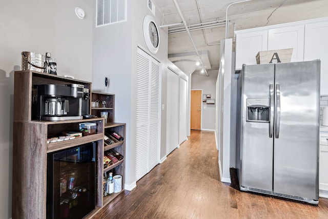 interior space with beverage cooler, wood finished floors, a towering ceiling, visible vents, and baseboards