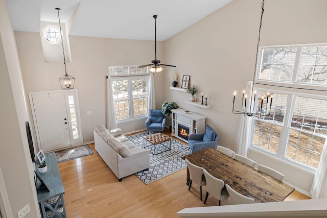 living room featuring light wood-style floors, a warm lit fireplace, high vaulted ceiling, and baseboards