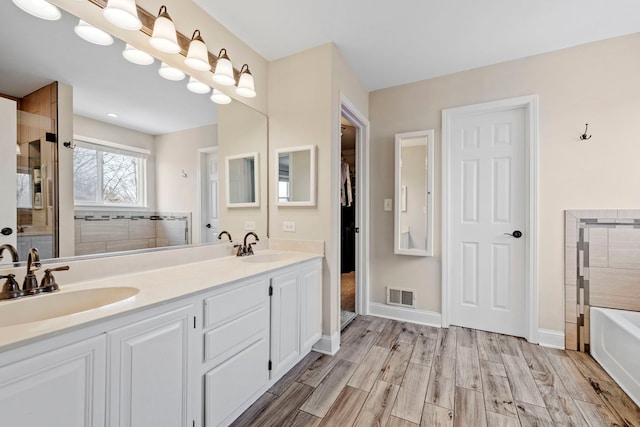 bathroom featuring a tub to relax in, wood finish floors, a sink, and visible vents