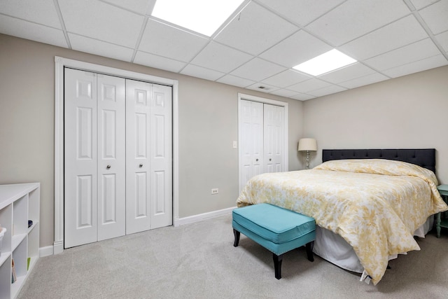 bedroom featuring baseboards, a drop ceiling, two closets, and carpet flooring