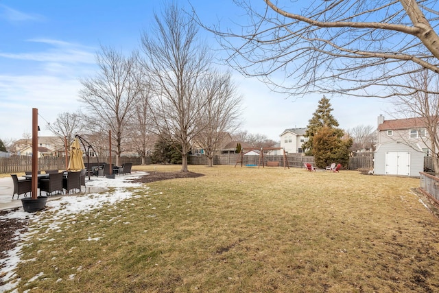 snowy yard featuring a fenced backyard, a residential view, an outbuilding, a storage unit, and a patio area