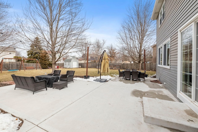 view of patio / terrace with a playground, a storage unit, outdoor dining space, a fenced backyard, and an outdoor structure