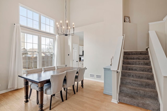 dining room with light wood finished floors, stairway, a towering ceiling, and an inviting chandelier