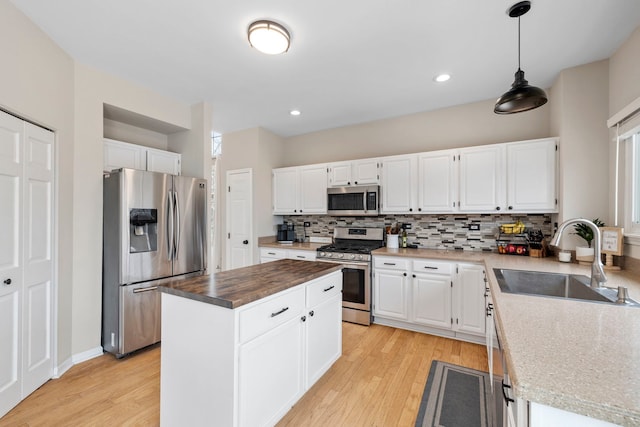 kitchen featuring light wood finished floors, decorative backsplash, a kitchen island, appliances with stainless steel finishes, and a sink