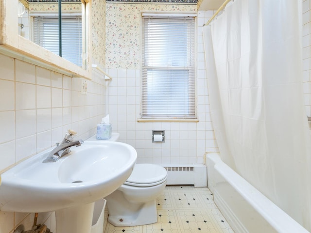 full bathroom with toilet, a sink, a baseboard heating unit, tile walls, and wallpapered walls