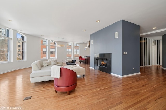 living area with recessed lighting, visible vents, hardwood / wood-style floors, a multi sided fireplace, and baseboards