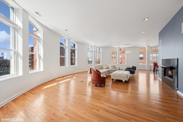 living room featuring recessed lighting, visible vents, light wood-style flooring, a glass covered fireplace, and baseboards