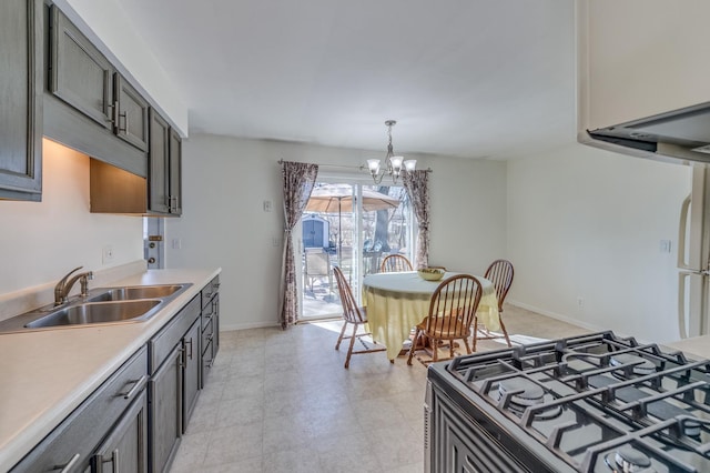 kitchen featuring baseboards, a sink, light countertops, range with gas cooktop, and a notable chandelier