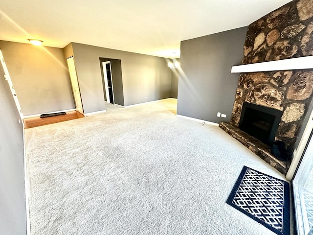 carpeted living room with a stone fireplace and baseboards