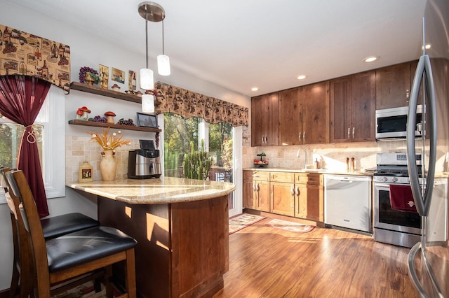 kitchen featuring decorative light fixtures, appliances with stainless steel finishes, light wood-style floors, a sink, and a peninsula