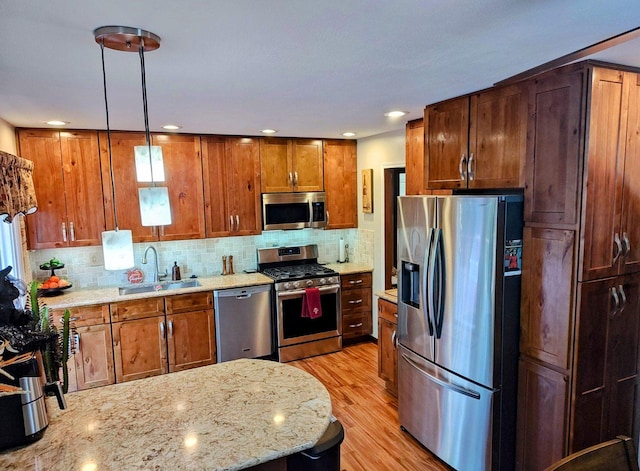 kitchen featuring light stone counters, stainless steel appliances, a sink, brown cabinetry, and decorative light fixtures