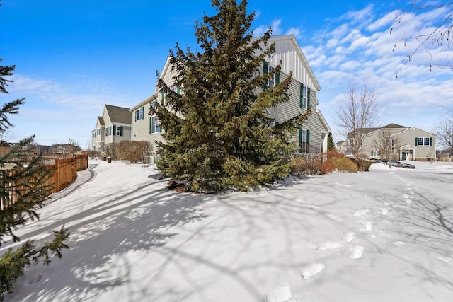 snow covered property featuring board and batten siding, a residential view, and fence