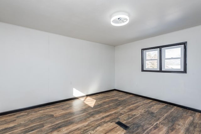 unfurnished room featuring dark wood-style floors, visible vents, and baseboards