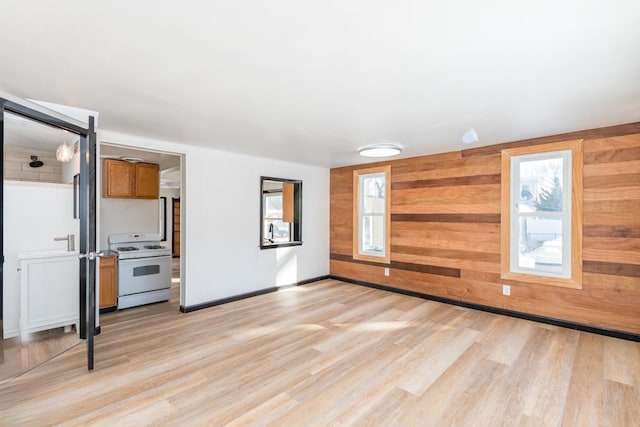 unfurnished living room featuring light wood-style flooring, a healthy amount of sunlight, and wooden walls