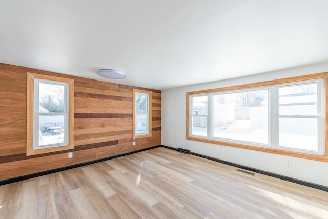 unfurnished room featuring wood walls, baseboards, visible vents, and wood finished floors