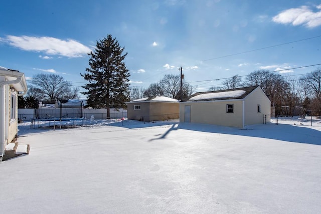 yard covered in snow featuring a trampoline, fence, and an outbuilding