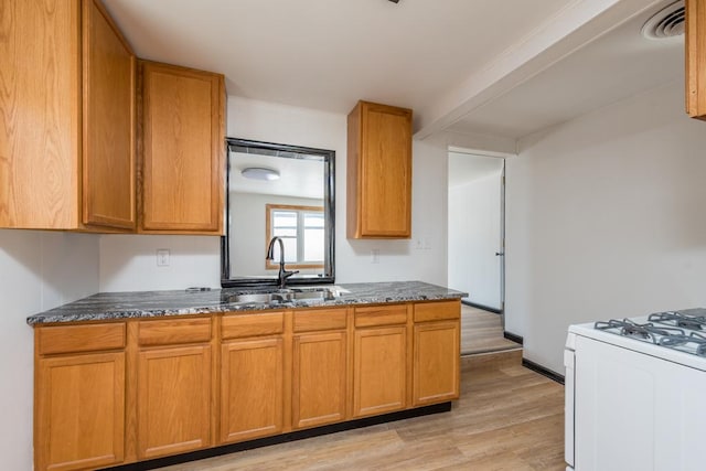 kitchen with white gas stove, a sink, light wood-type flooring, brown cabinets, and dark stone counters