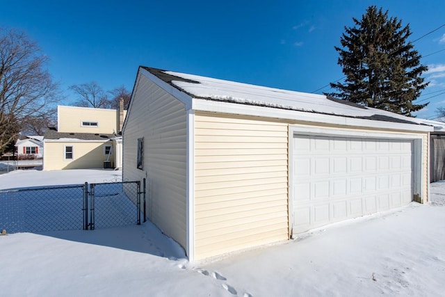 snow covered garage featuring a detached garage, a gate, and fence