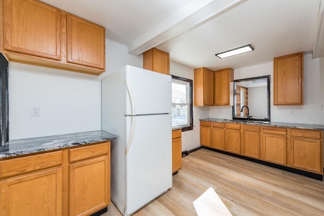 kitchen featuring stone counters, a sink, light wood-style floors, freestanding refrigerator, and brown cabinets