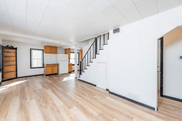 unfurnished living room with light wood finished floors, visible vents, stairway, and baseboards