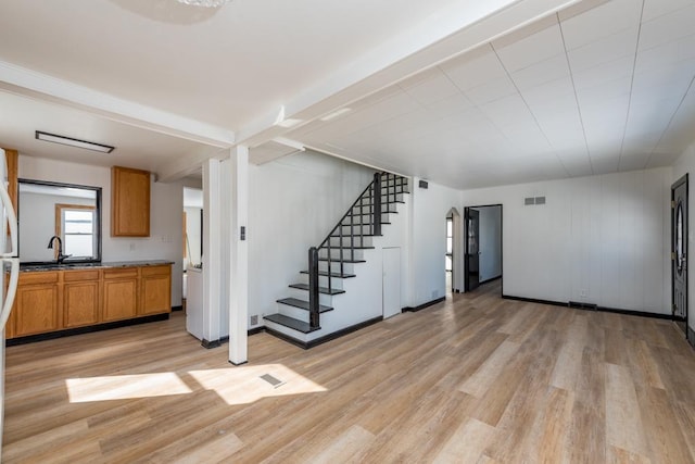 unfurnished living room with stairs, light wood-style flooring, a sink, and visible vents