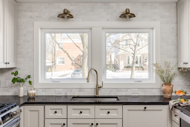 kitchen featuring tasteful backsplash, dark countertops, a sink, and white cabinetry