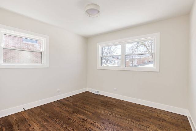 empty room featuring dark wood-type flooring, visible vents, and baseboards