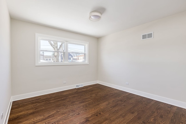 spare room featuring dark wood-type flooring, visible vents, and baseboards