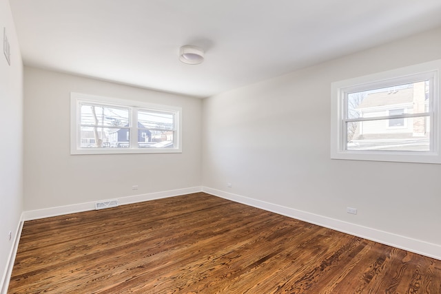 empty room featuring dark wood-style flooring, visible vents, and baseboards