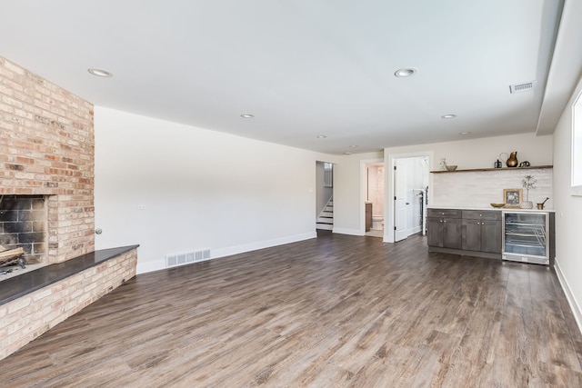 unfurnished living room featuring visible vents, stairway, a brick fireplace, wood finished floors, and beverage cooler