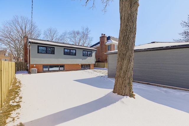 view of front facade featuring brick siding, a chimney, fence, and central air condition unit